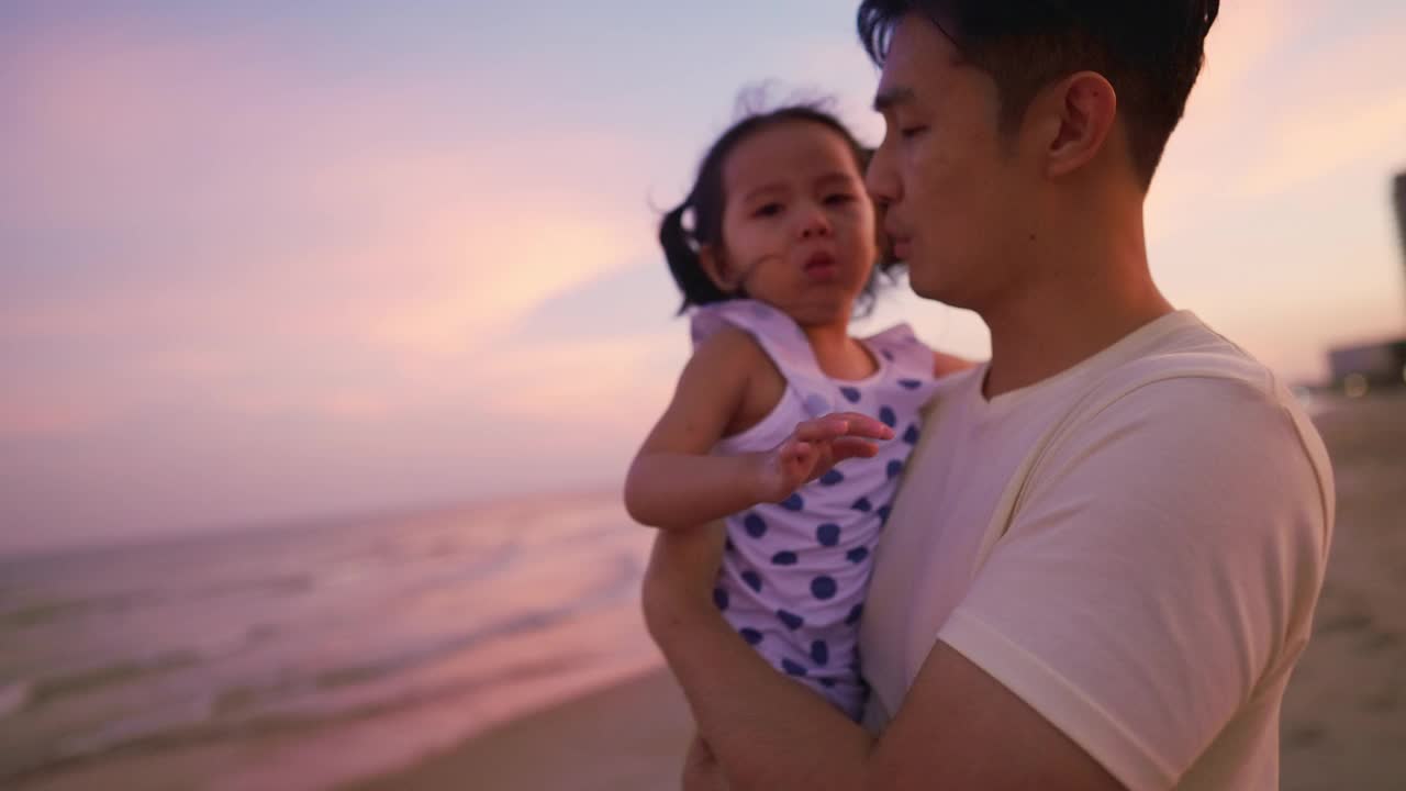 亚洲父亲抱着女儿在空中，而散步在海滩上的黄昏时间度假。视频素材