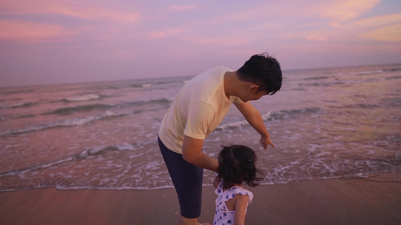 父亲边走边指着海滩，在黄昏时分教他的女儿。视频素材