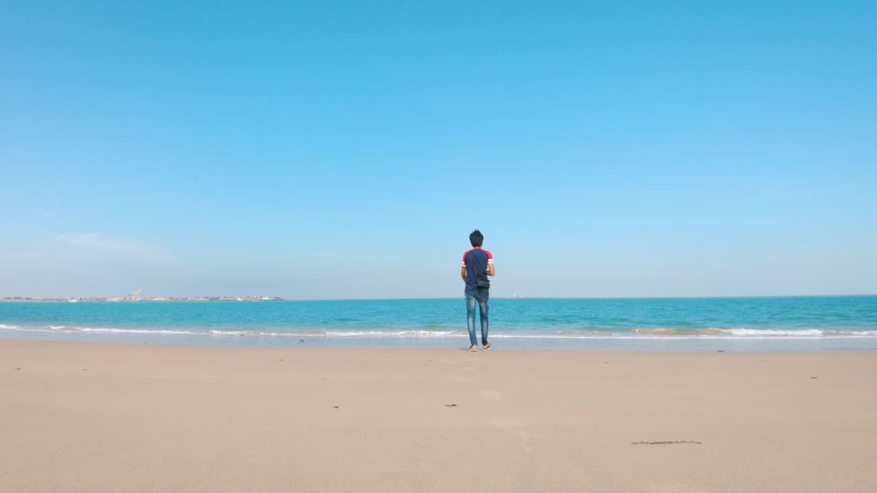 在印度古吉拉特邦的Bet Dwarka，一个年轻的印度男子在海滩上朝着大海走去。夏日放松海滩背景视频素材