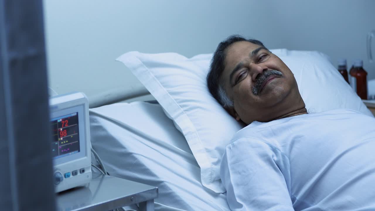 中镜头的生病成熟男子微笑和交谈，而躺在医院的床上视频下载