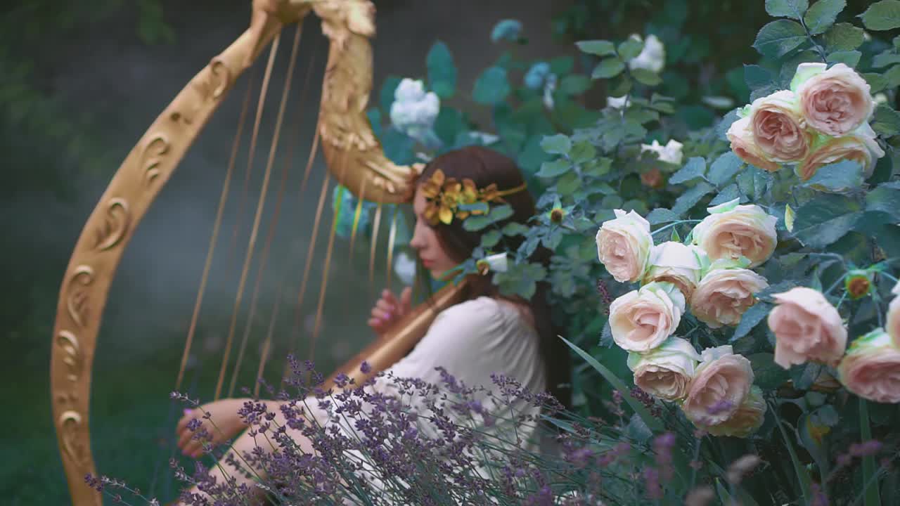精灵女孩弹奏着古老的金色竖琴。公主在春天开花的花园里。视频素材