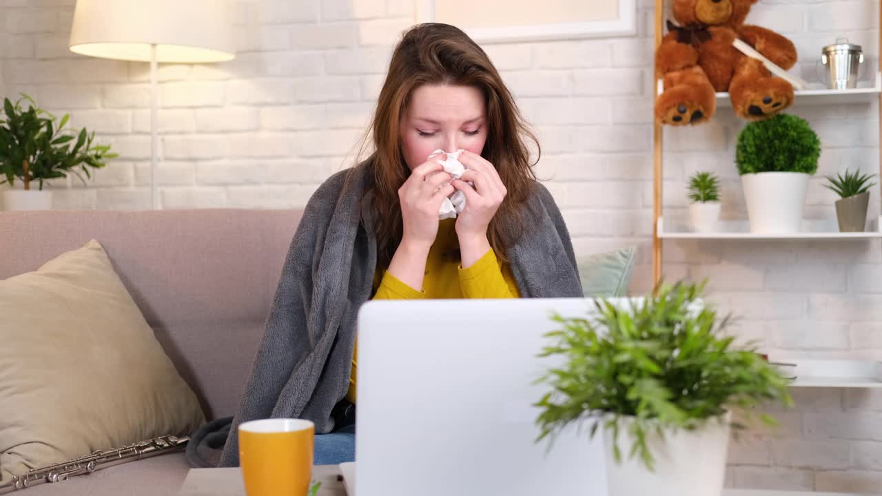 一个女人用笔记本电脑打视频电话，和医生聊天，用手帕擤鼻子。视频下载