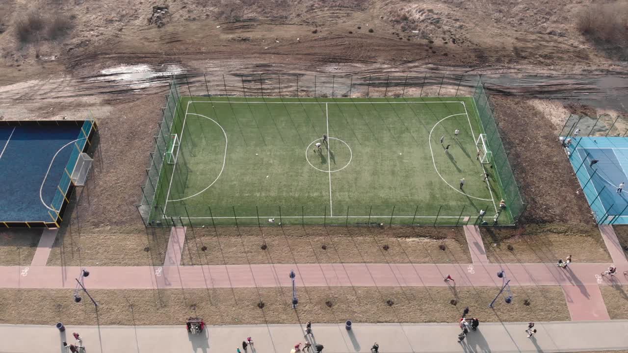 一群活跃的年轻人在现代足球场上踢足球。在城市步行街上有运动场地和游戏区。积极的生活方式视频素材
