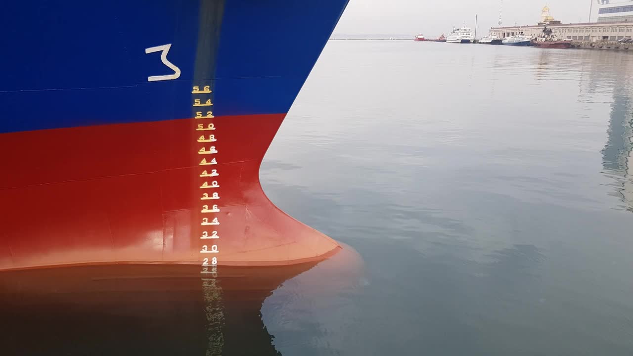 风平浪静时船首的红色。一艘蓝色的船停泊在港口的岸边，正在装卸货物。视频下载