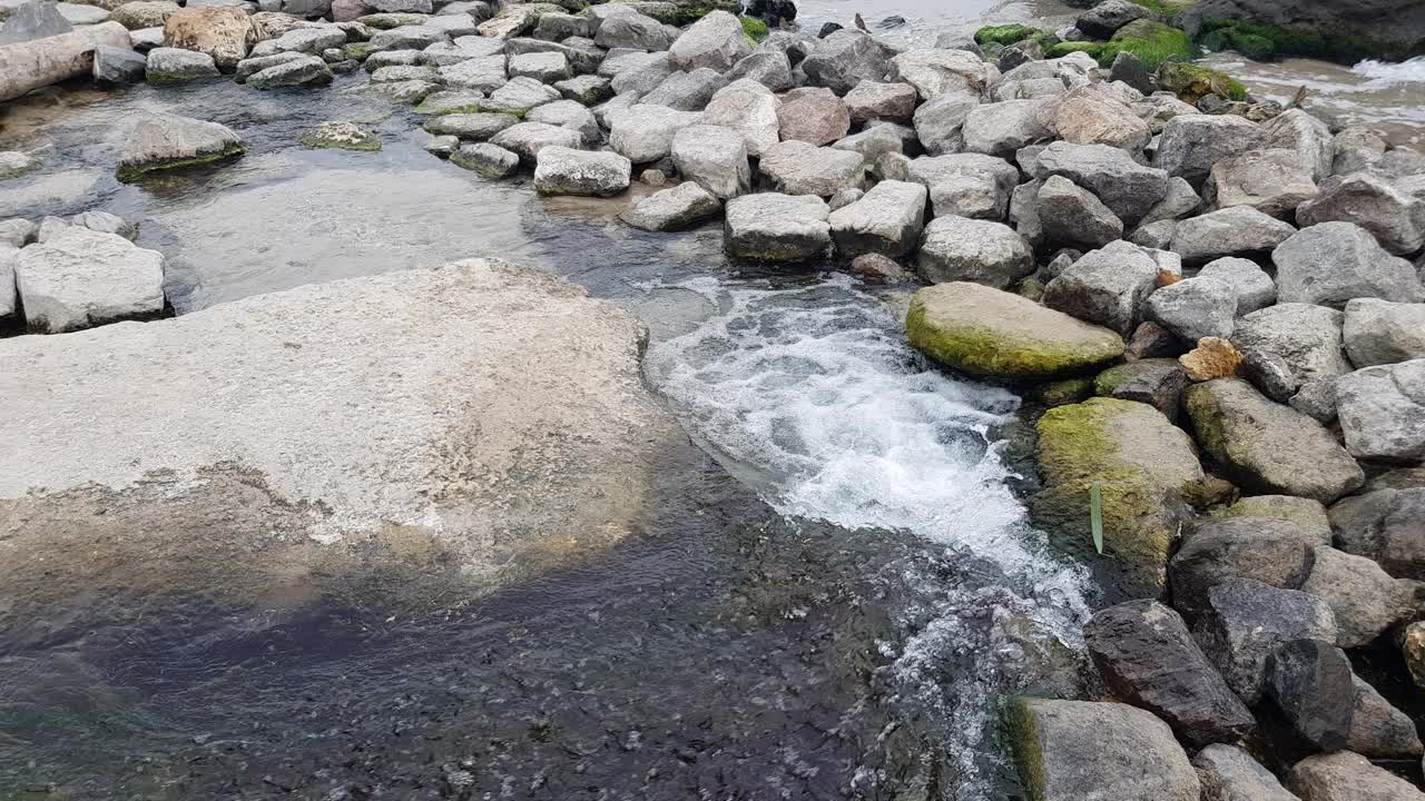 一股清流从石头中泻下，流入大海。视频下载