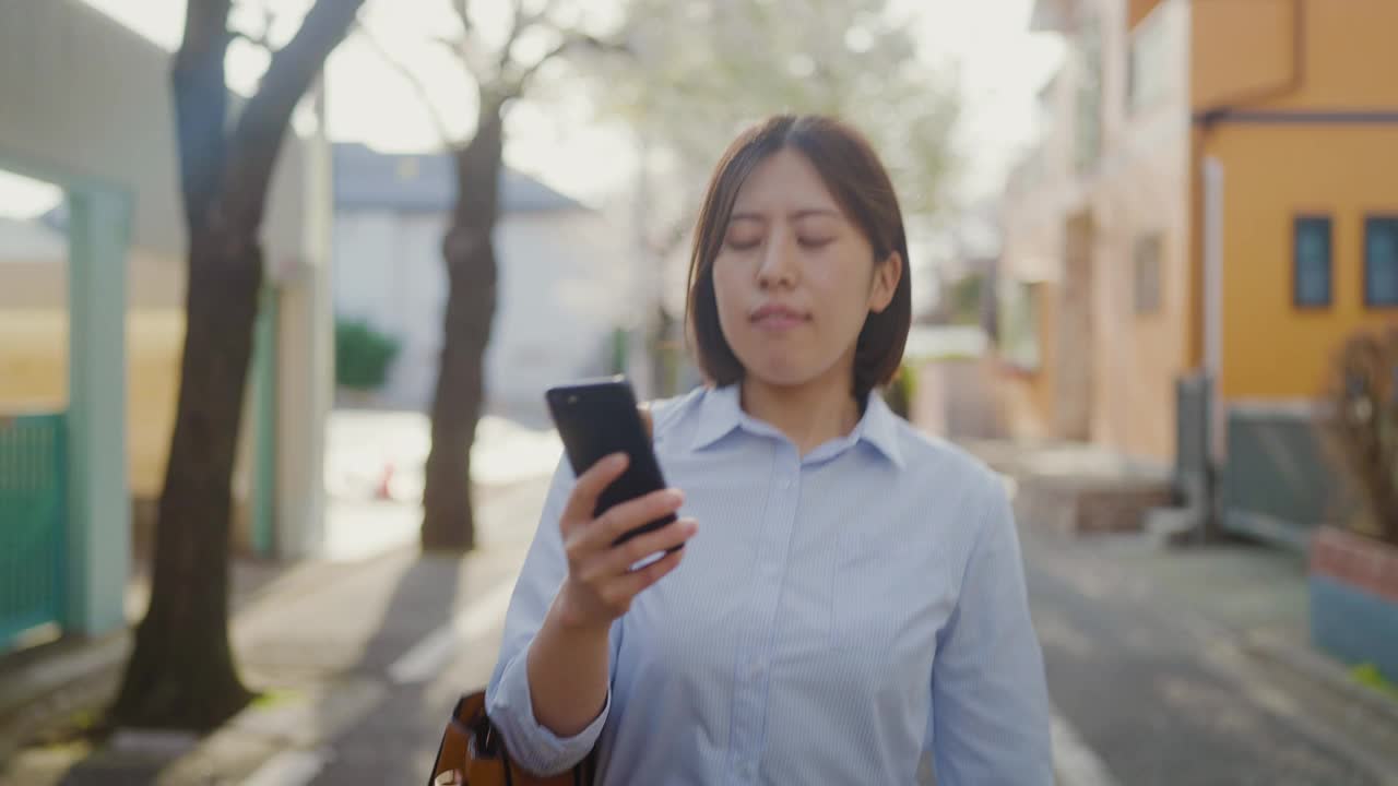 年轻的女商人使用智能手机，在城市樱花树下通勤工作视频素材