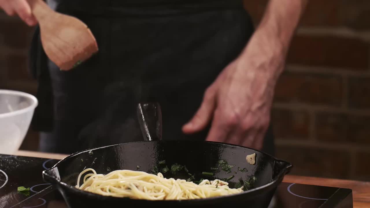 厨师在餐厅厨房里把意大利面和炸蘑菇、大蒜和欧芹放在煎锅里。食品成分。。准备吃的食物。意大利烹饪。美味的晚餐视频素材