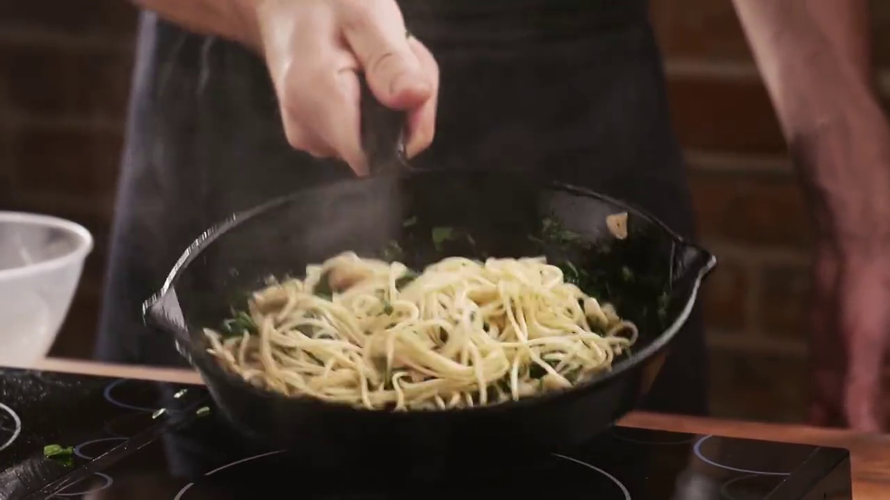 在家庭厨房里，一名男子在平底锅中将意大利面与炸蘑菇、大蒜和欧芹混合在一起。在家做意大利面视频素材