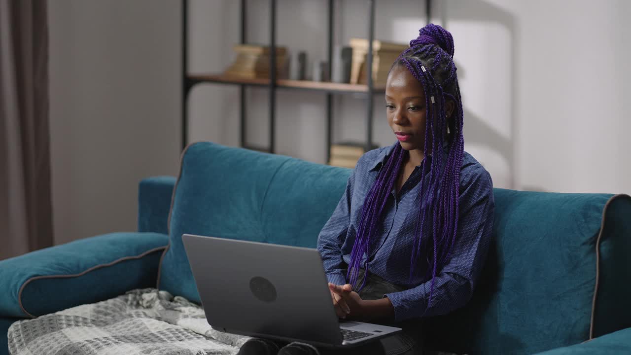 遥远的工作面试的年轻黑人妇女通过视频会议在笔记本电脑，妇女是坐在沙发上，把笔记本电脑放在膝盖上视频素材