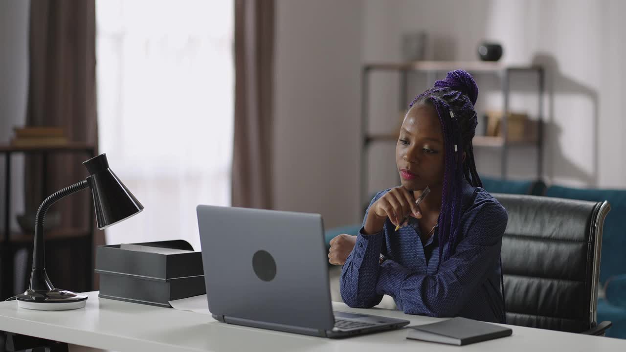 一位非裔美国妇女正在看笔记本电脑屏幕，听学习网络研讨会或在线讲座视频素材