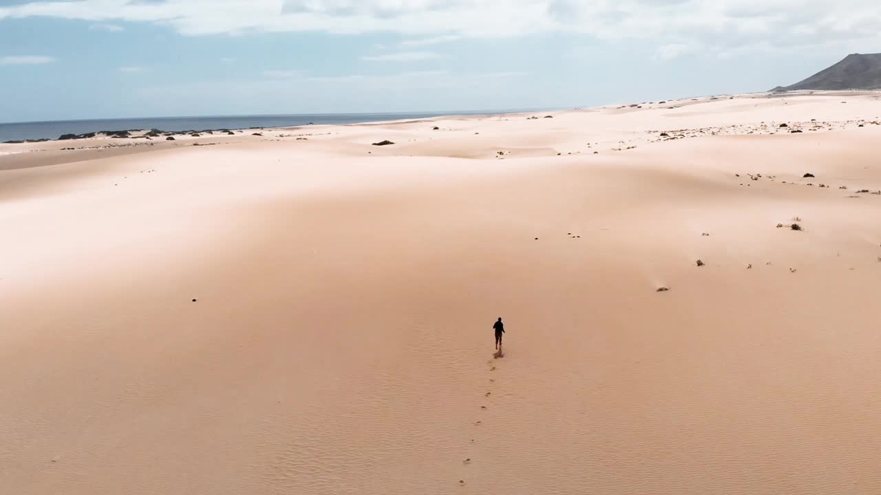 无人驾驶飞机在富埃特文图拉岛的沙丘沙漠里跟踪一个赤脚奔跑的人。西班牙。视频下载