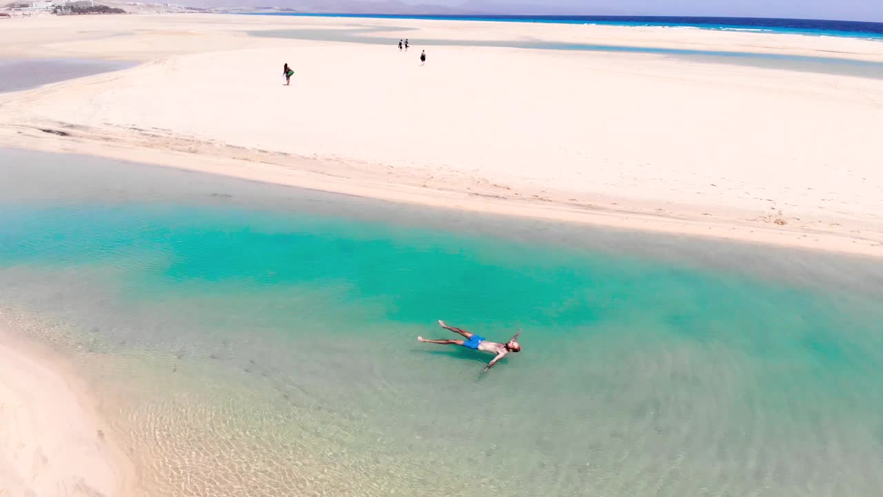 在富埃特文图拉岛的天堂海滩上，一个家伙漂浮在绿松石泻湖上。西班牙。视频素材