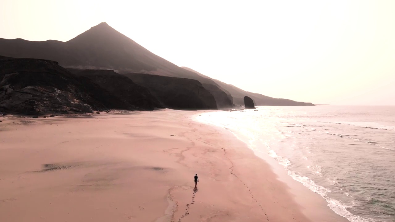 在福埃特文图拉岛，一名男子在日落时走在天堂海滩上的无人机镜头。西班牙。视频素材