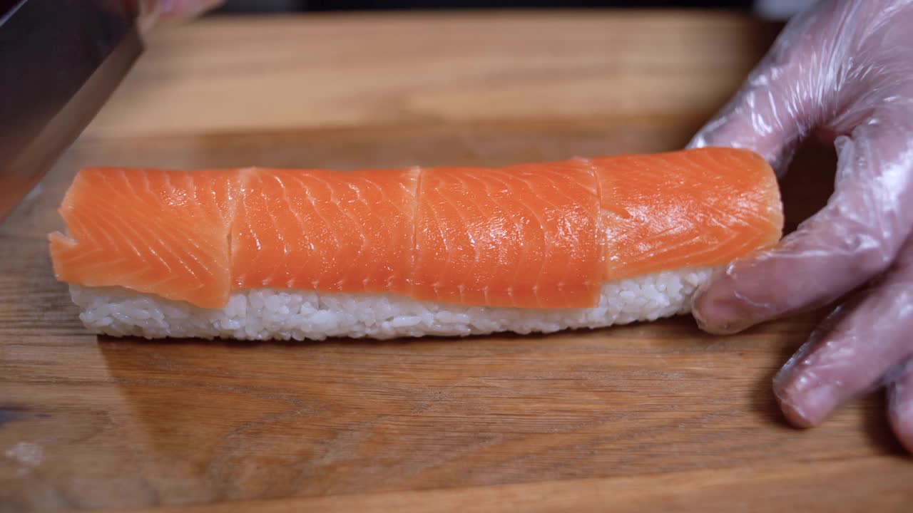 男性用手将金枪鱼寿司卷在砧板上切成两半。切寿司卷。视频下载