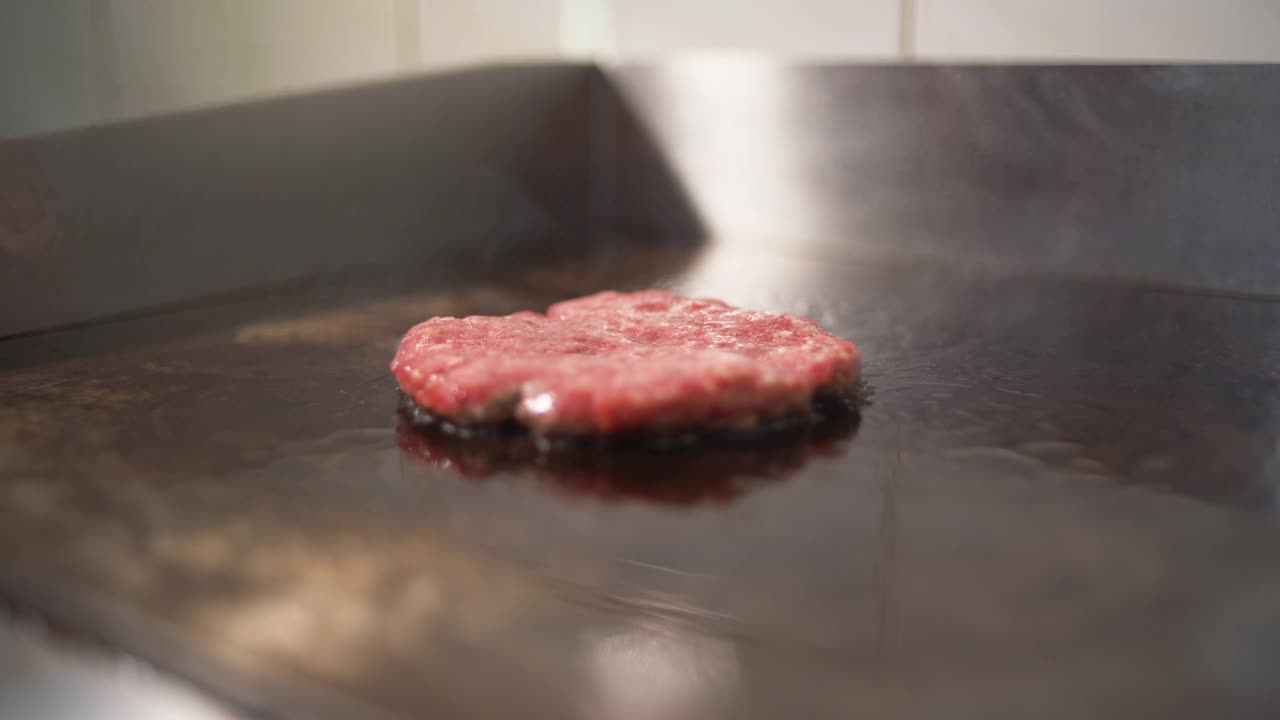 做一个汉堡的牛肉和猪排。肉在厨房里烤。厨师用铲子把肉翻过来。视频素材