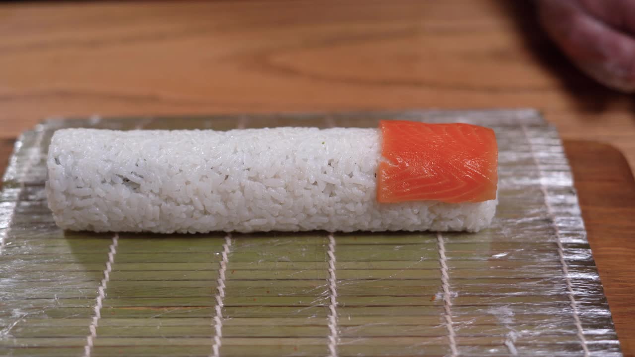 一位专业厨师将切成薄片的三文鱼放到餐桌上的寿司卷上。在一家日本餐厅，男厨师正在准备一个三文鱼寿司卷。视频下载