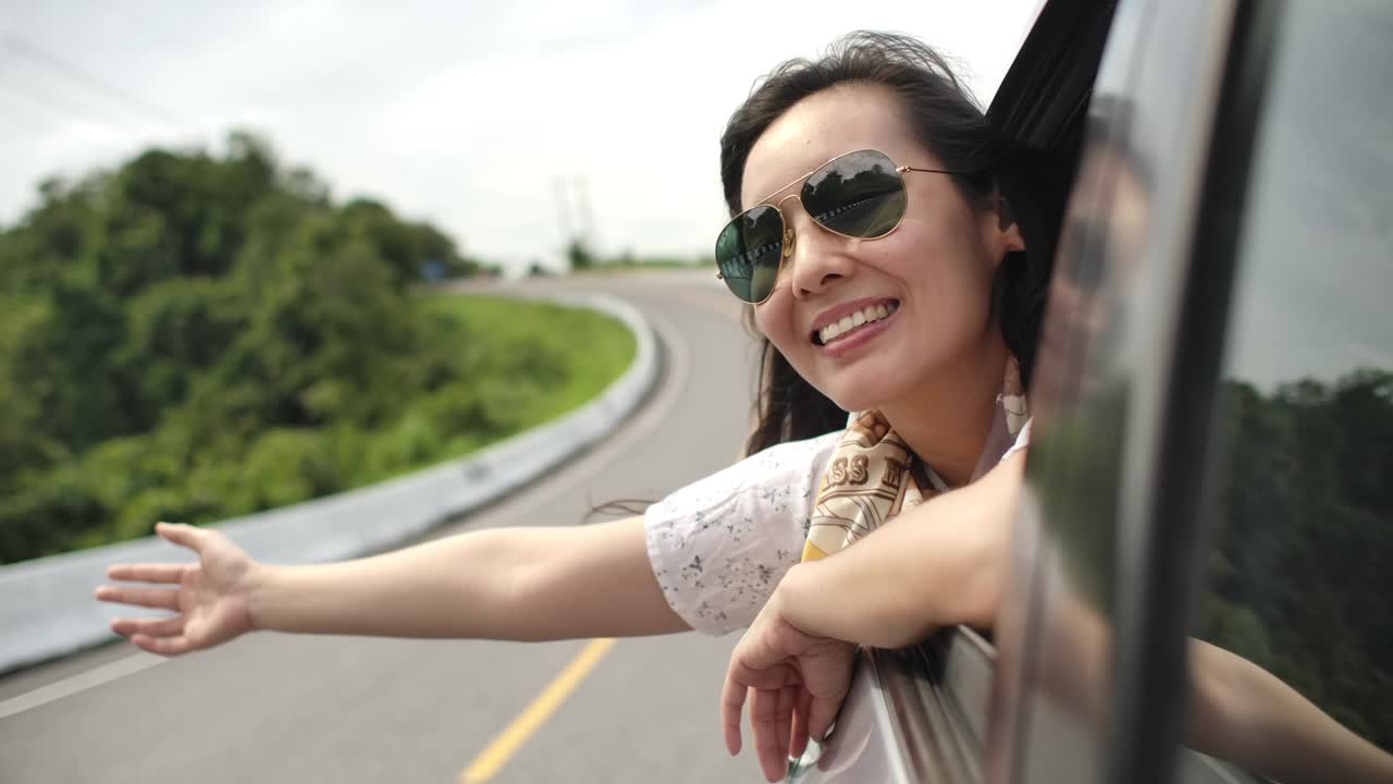 一个亚洲女人把她的手伸出车窗，笑了。慢动作视频素材