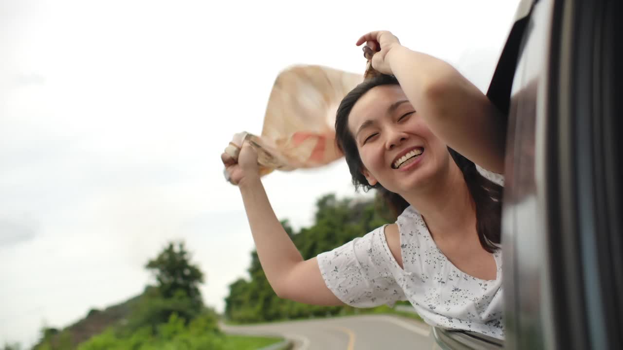亚洲妇女伸出车窗，享受风景和风在她的头发视频素材