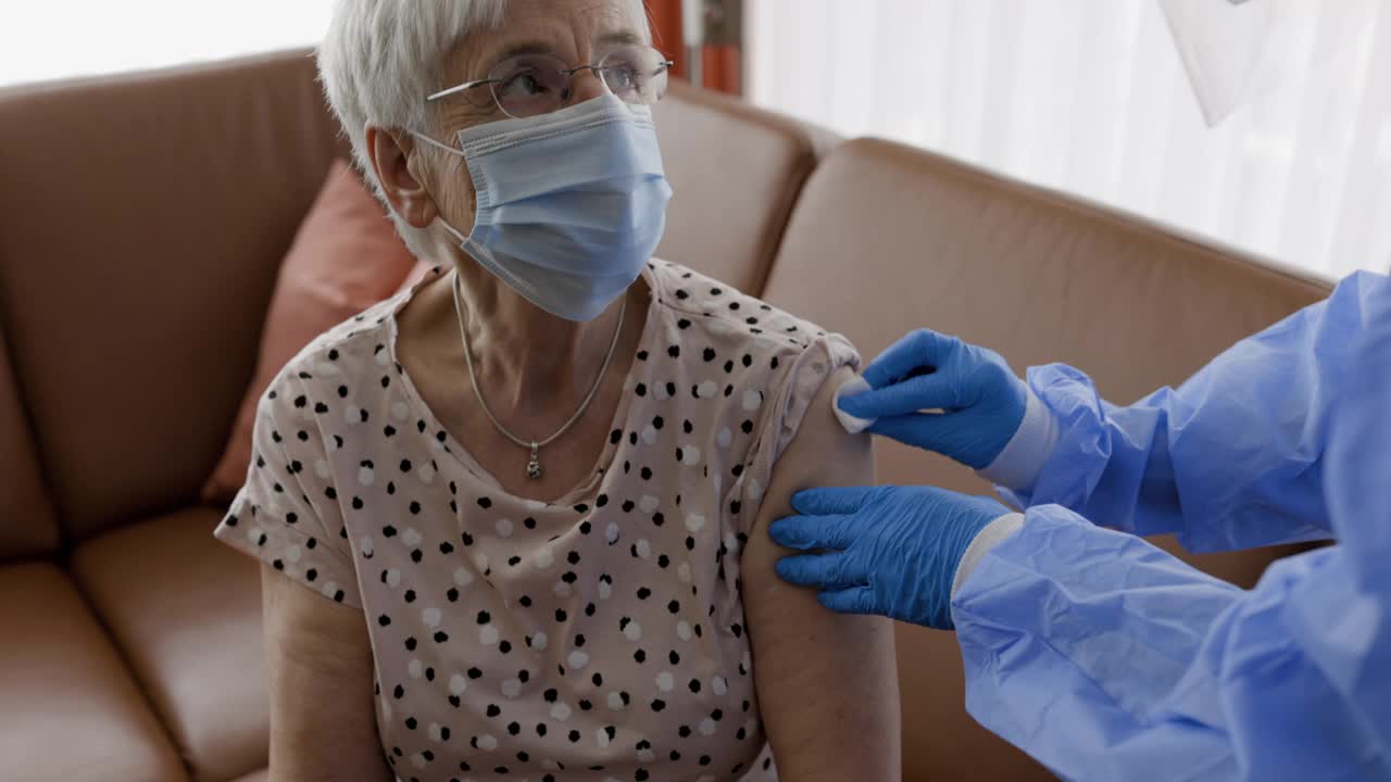 年长妇女戴着口罩在家接种疫苗视频素材