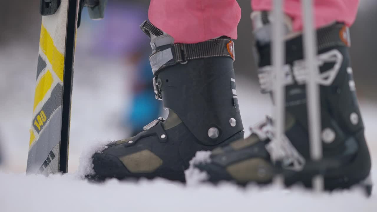 滑雪靴上的女性腿在户外的特写。一个面目全非的女人站在滑雪场的雪地里。冬季运动和旅游概念。视频下载