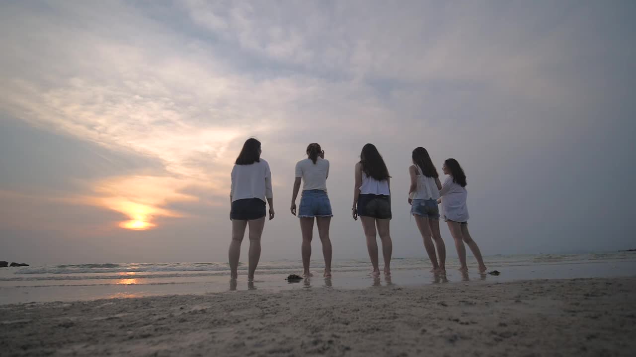 一群朋友欢天喜地，在沙滩上跳跃着落日的剪影视频素材
