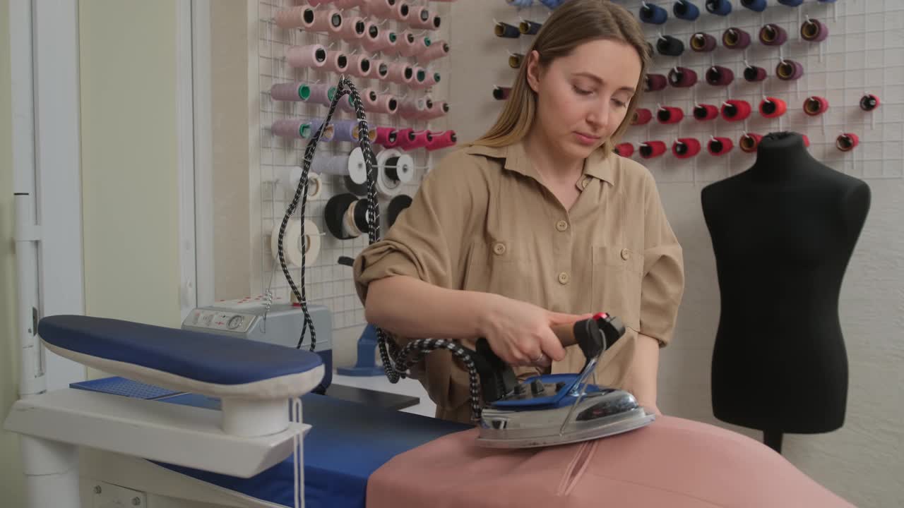 一位时装裁缝设计师在缝纫车间用熨斗和蒸汽熨烫衣服。服装的生产。缝纫产品在服装业务。视频素材