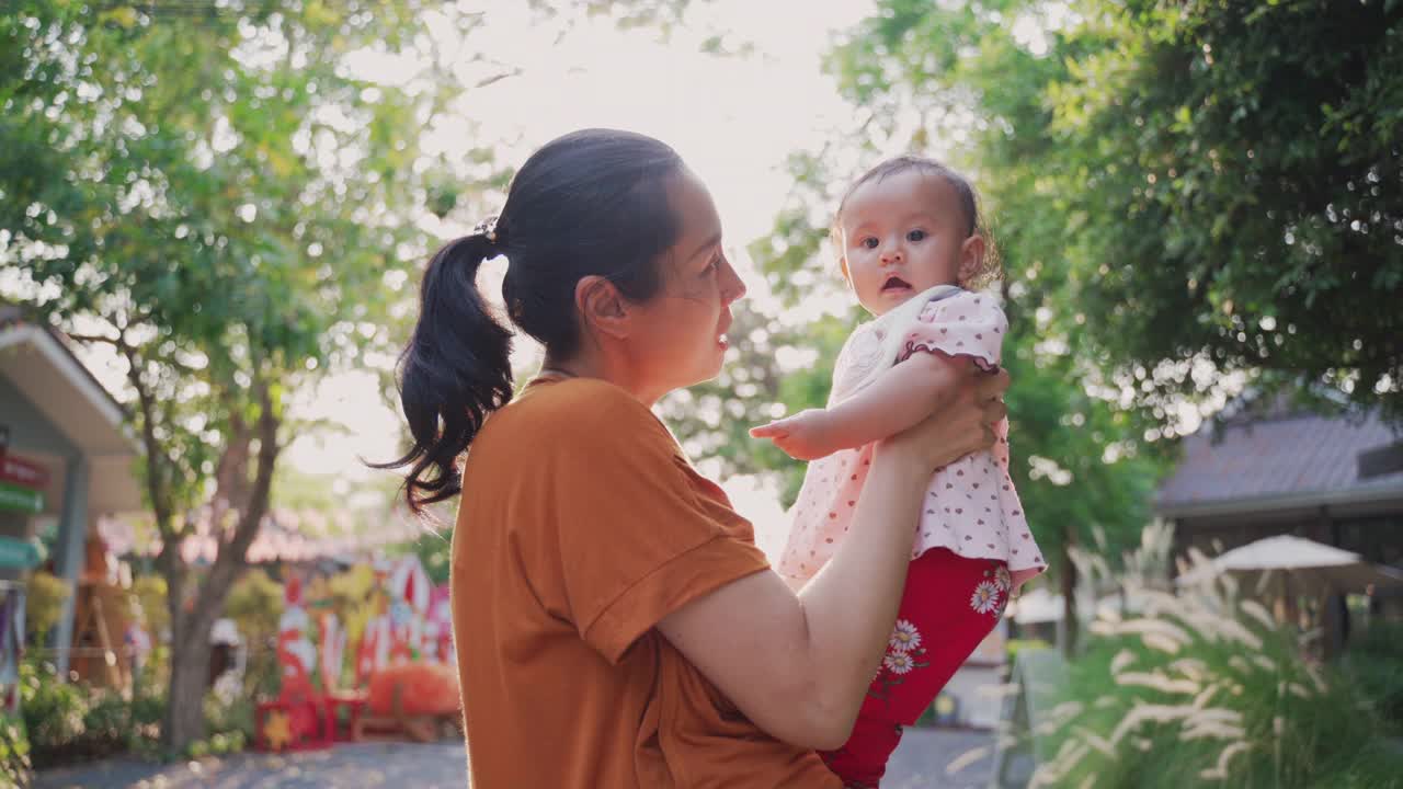 亚洲单身母亲在花园中高举双手，亲吻她的孩子视频素材