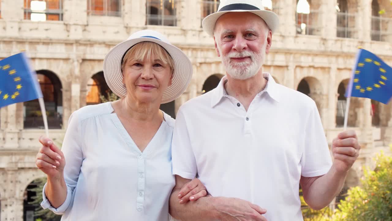 一对愉快的老年夫妇在罗马度假。罗马竞技场附近的养老金领取者挥舞着欧盟旗帜视频下载