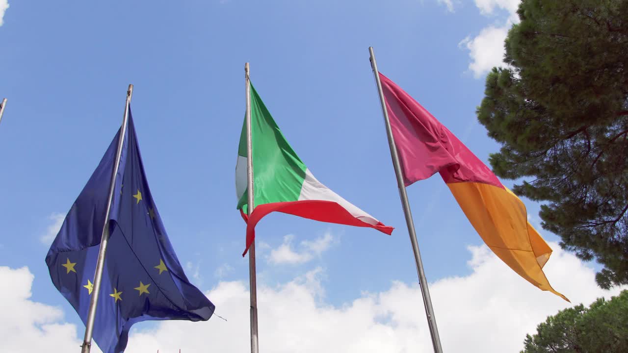 三面旗子迎风飘扬，映衬着蓝天。近距离观察意大利欧盟和意大利罗马城的旗帜视频下载
