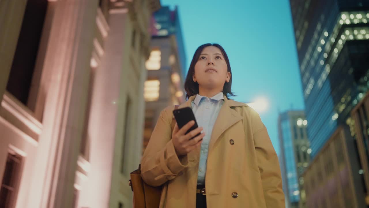 年轻的女商人拿着她的智能手机在城市的金融区通勤视频素材