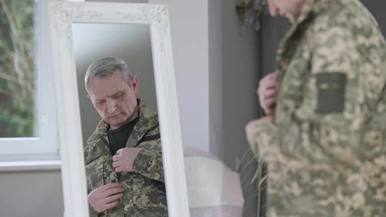 自信英俊的中年男子在室内调整军装的镜子中映照。一幅严肃的白人士兵在家伪装的照片。步兵服务。视频素材