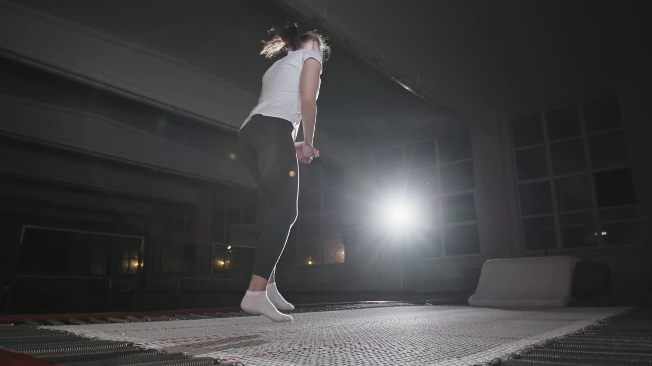 2019年9月29日，乌克兰，Ternopil:女子体操运动员在一个黑暗的健身房里，在一盏明亮的聚光灯下，用手在蹦床上跳跃，进行政变练习视频下载