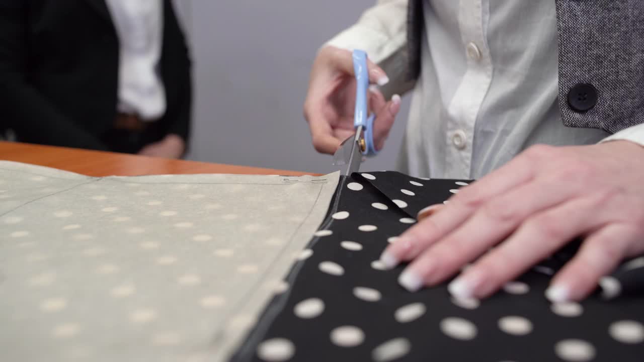 修指甲的时候，女裁缝用特制的缝纫剪刀把黑色带白色圆点的布料剪下来。缝纫车间。视频素材