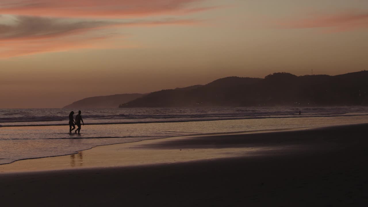 远处一对夫妇的剪影在日落的海洋海滩上散步/圣布拉斯，拉利伯塔德，萨尔瓦多视频下载