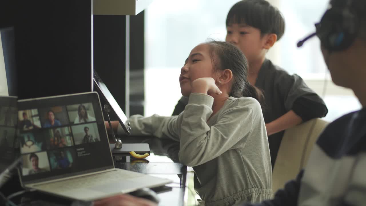 Lifehack亚洲华人父亲在家工作，用耳机与同事视频通话，而他的孩子在他旁边使用数字平板电脑视频下载