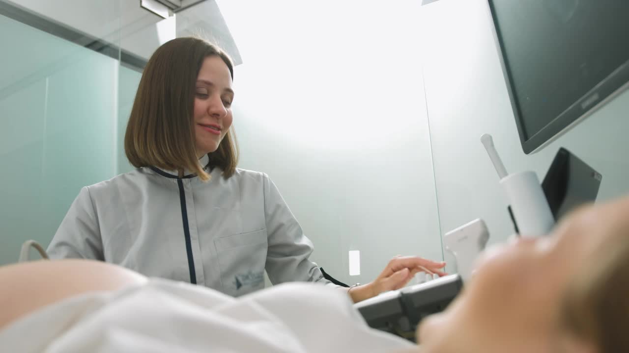 年轻的微笑专业迷人的女医生在做3d超声孕妇的腹部在诊所。孕妇超声波检查。咨询师，和病人交谈视频素材