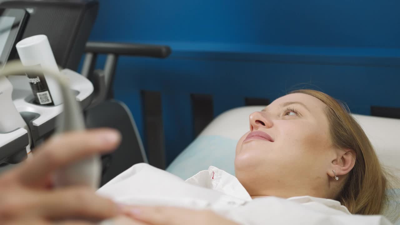 近距离医生的手，使用现代超声设备筛查孕妇的腹部。快乐的孕妇躺下接受超声波检查视频素材