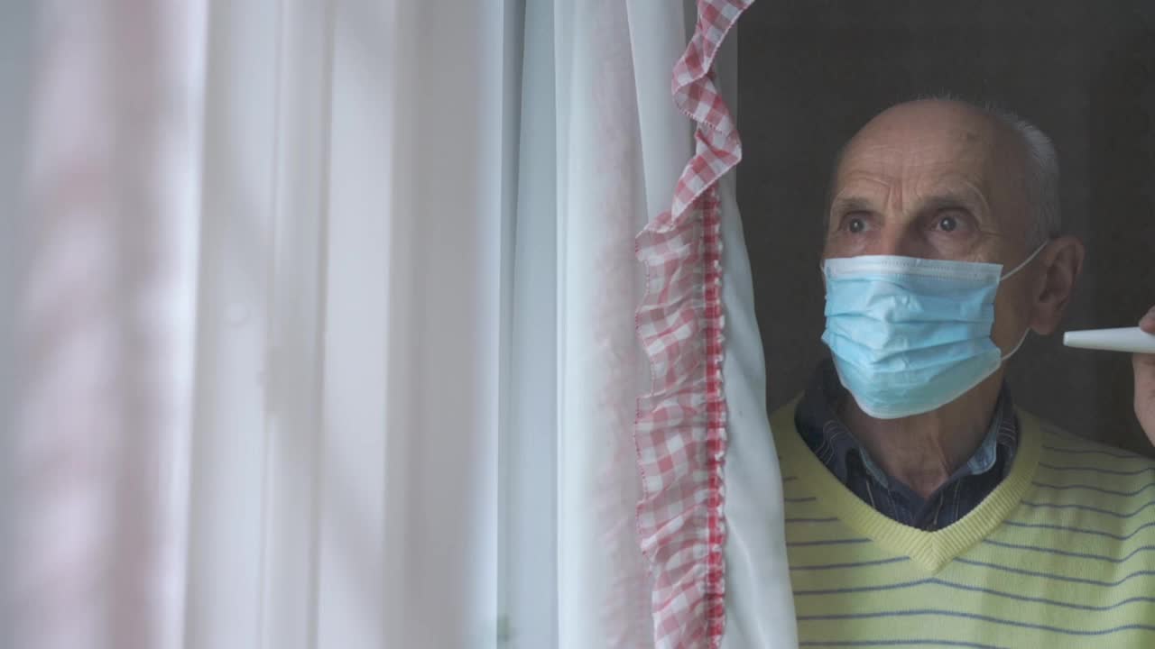 一位戴着蓝色面罩的老人站在塑料窗前视频素材