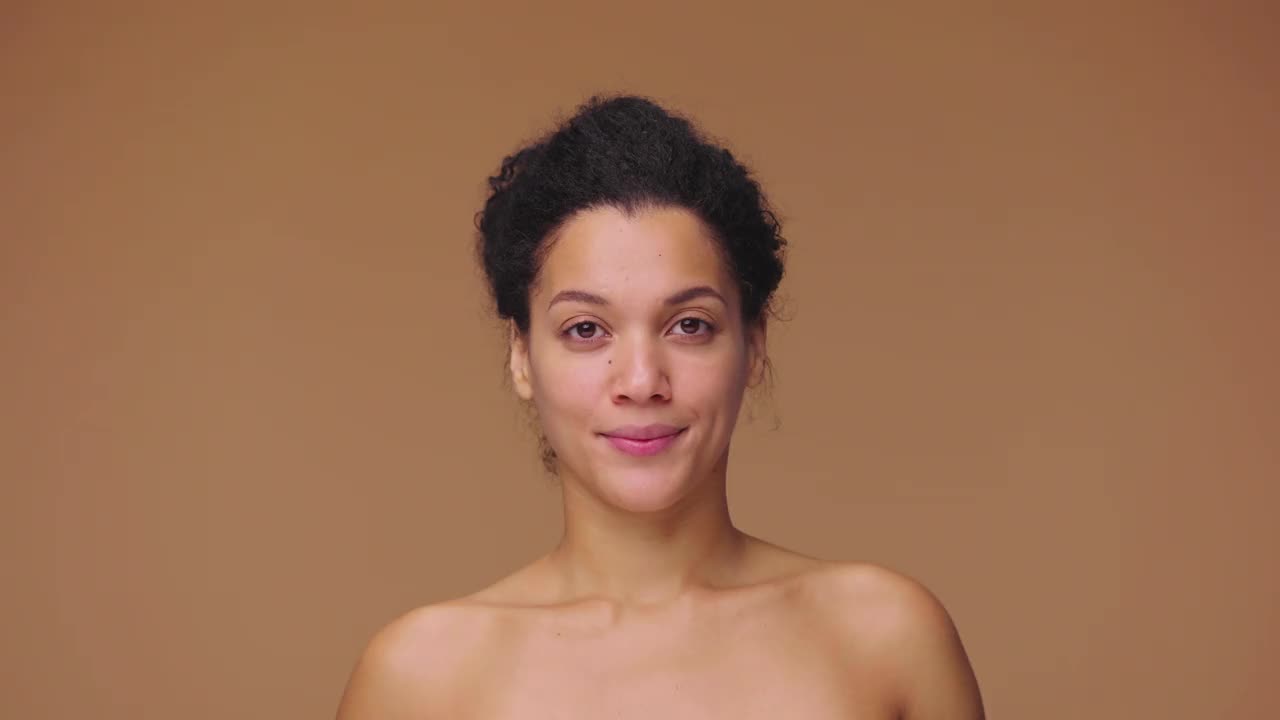 美丽肖像年轻的非裔美国妇女拿着半个鳄梨和面霜，自然护肤。黑人女性在棕色的工作室背景。慢动作准备，4K, 59.94fps视频下载