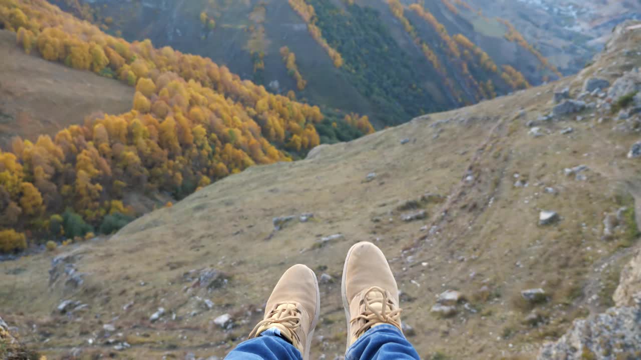 一个人坐在绿色山谷的高悬崖上摇摆双腿视频素材