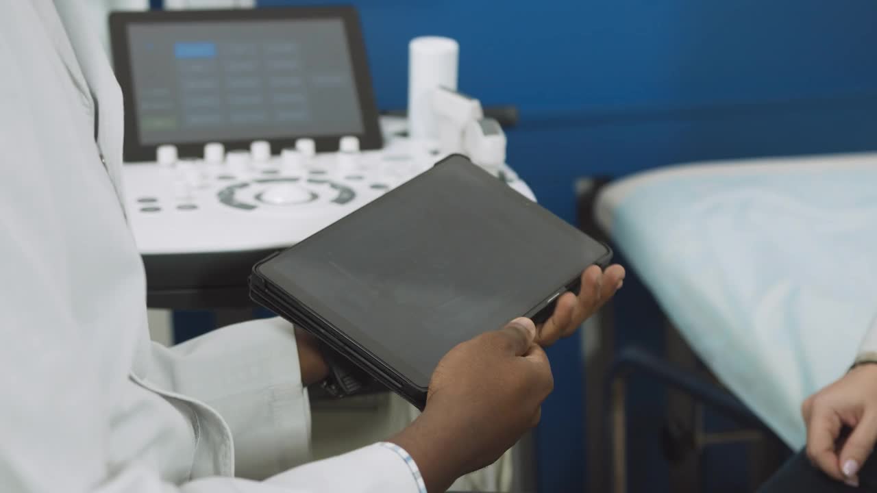 一名非洲男性医生向坐在沙发上的孕妇展示了带有婴儿超声波图像的数字平板电脑。专注于平板电脑视频素材