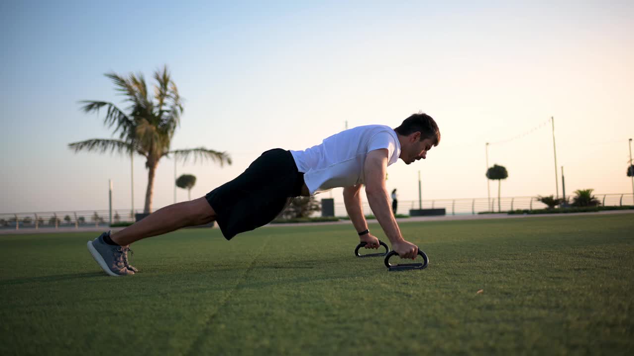 一名男子在公园的草地上做俯卧撑，在日落时分进行户外锻炼视频下载