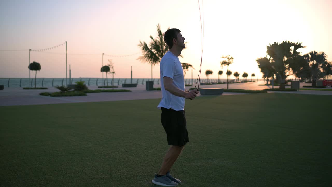 日落时分，一名男子在海边的公园里进行跳绳运动视频下载