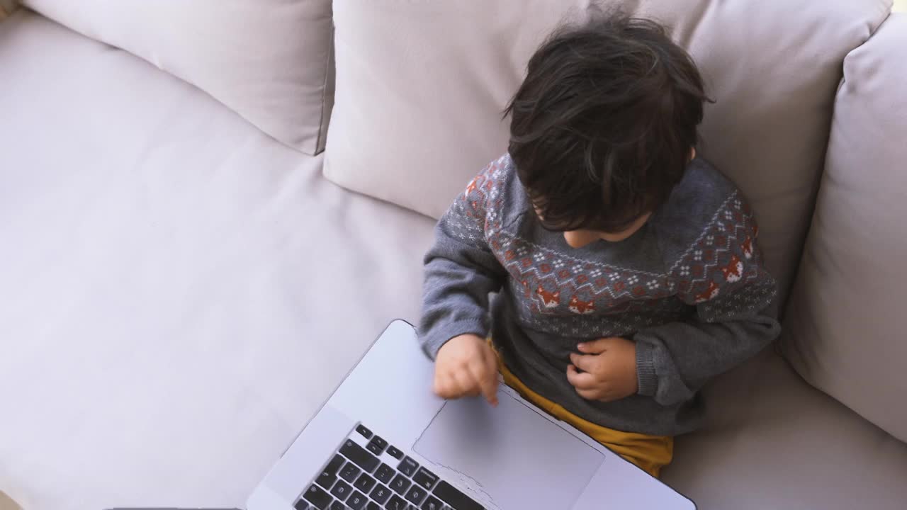 可爱的小男孩坐在阳台的沙发上使用笔记本电脑视频素材