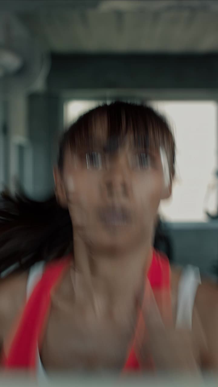 女子在跑步机上快速跑步的垂直视频。视频素材