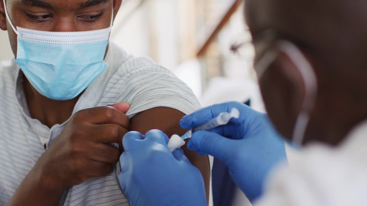 非裔美国资深男医生，戴口罩在家为男性患者接种covid - 19疫苗视频素材