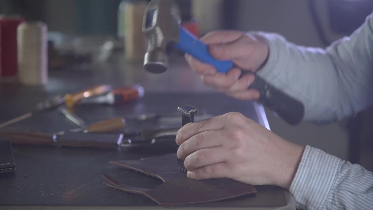 工匠的手在小块皮革上用工具和锤子打洞的特写镜头。工匠创造一个DIY的产品。手工工艺制造。手工工艺。视频素材