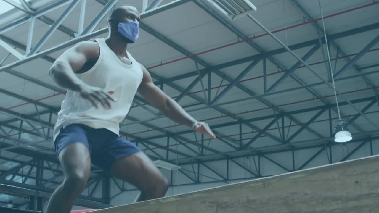 游戏界面对非洲裔美国人戴着面具跳上plyo盒在健身房视频下载
