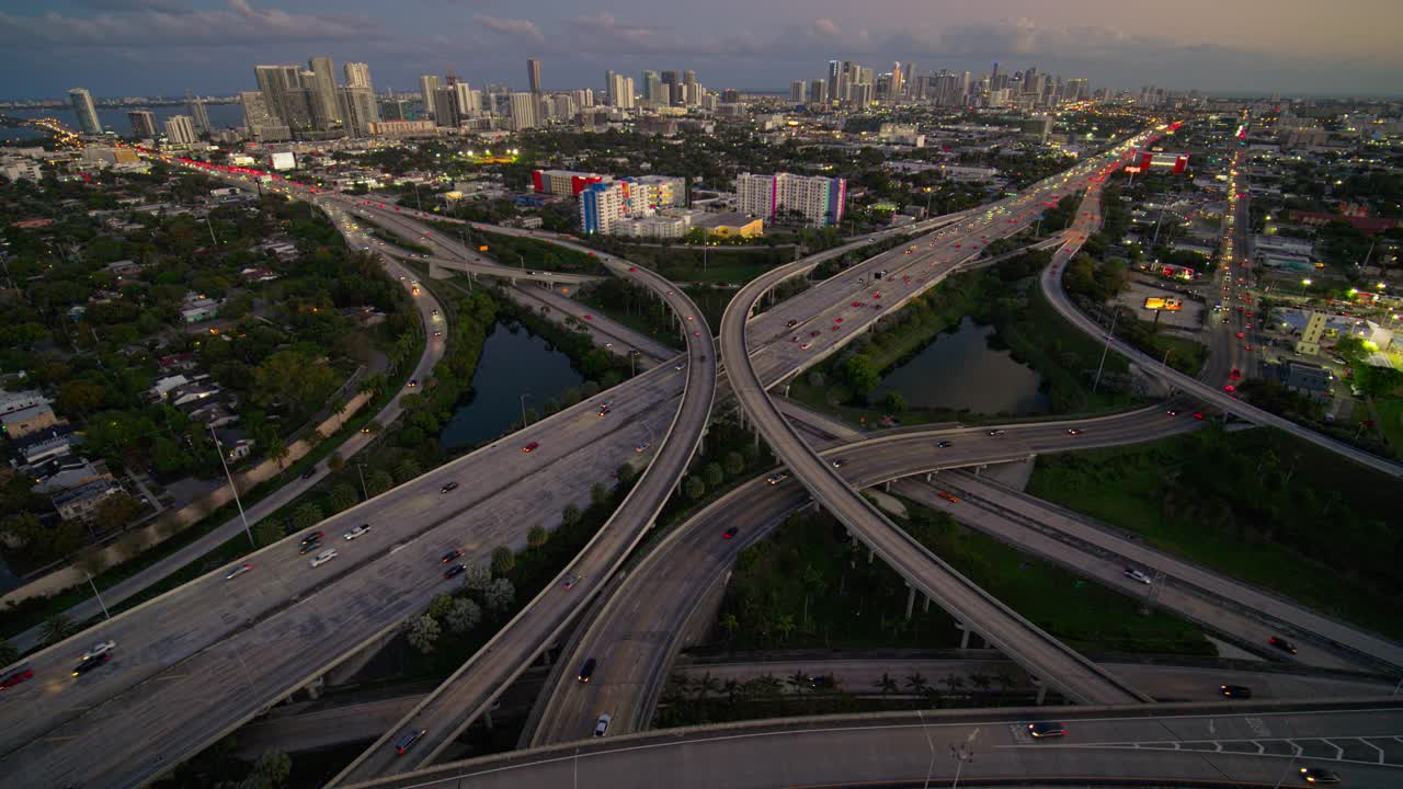 在北迈阿密，95号州际公路和I-195号公路之间繁忙的高架交通枢纽，日落时分，用超宽镜头拍摄的迈阿密市区和设计区远处的景象。无人机拍摄的b-roll镜头和下降的摄像机动作。视频下载