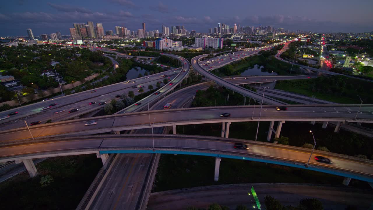 大而繁忙的高架交通枢纽州际95和I-195在北迈阿密，与设计区和迈阿密市中心的远程视图，在夜晚，用超宽镜头，无人机制作的b-roll镜头与下降的摄像机运动。视频下载